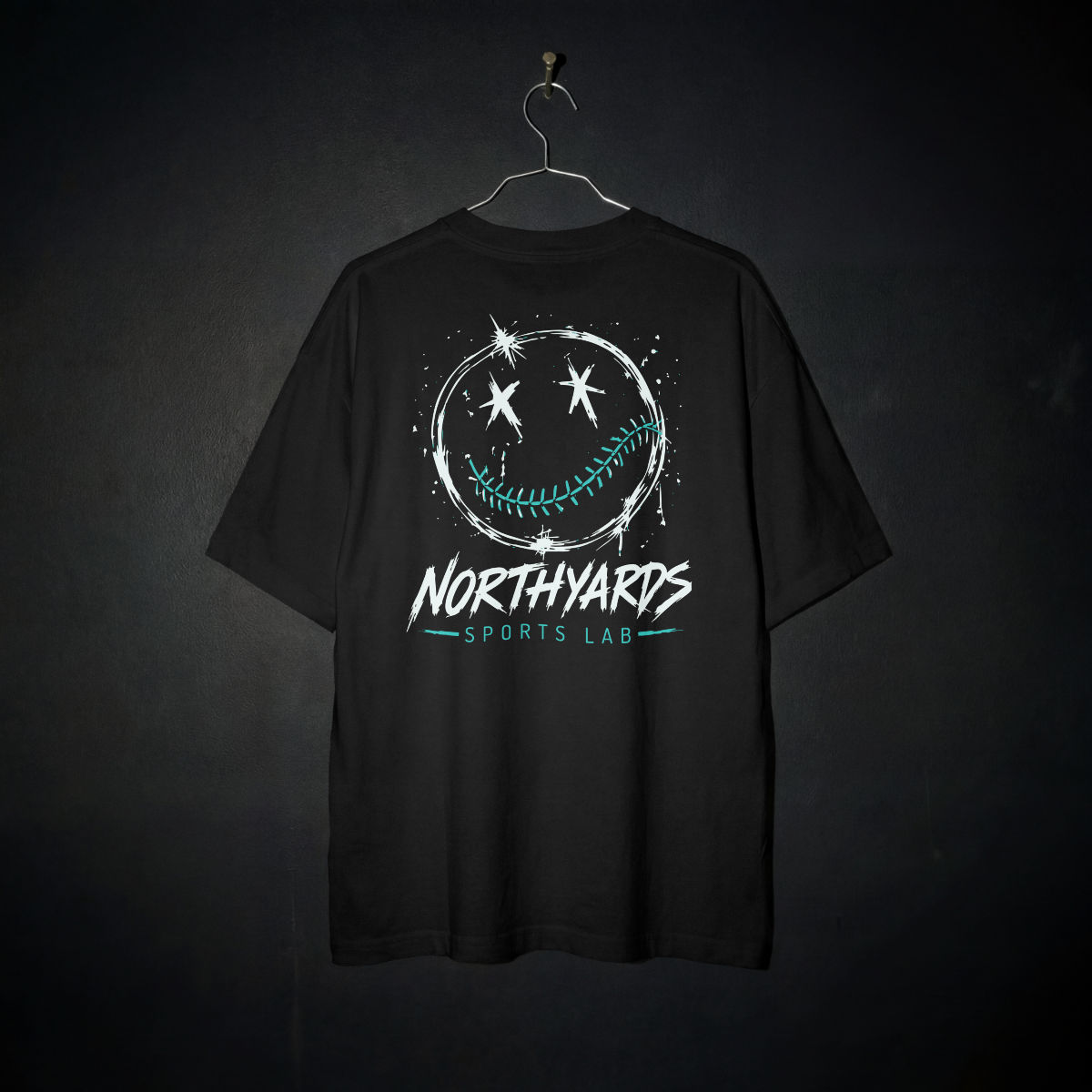 Smiley 1.0 Tee back – distressed white smiley face with crossed-out eyes and teal baseball-stitched smile above Northyards Sports Lab lettering